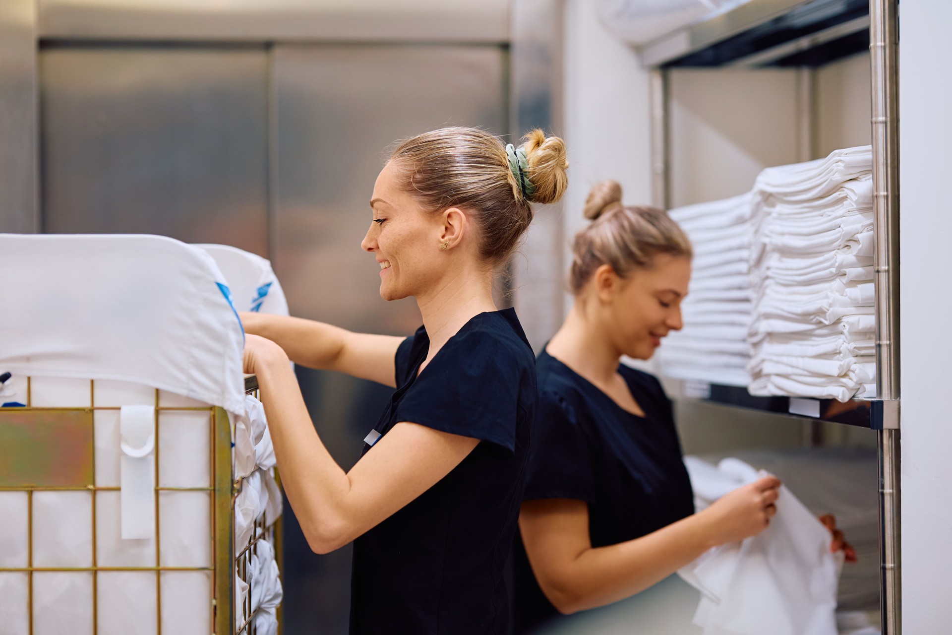 Happy maids working in hotel laundry room.