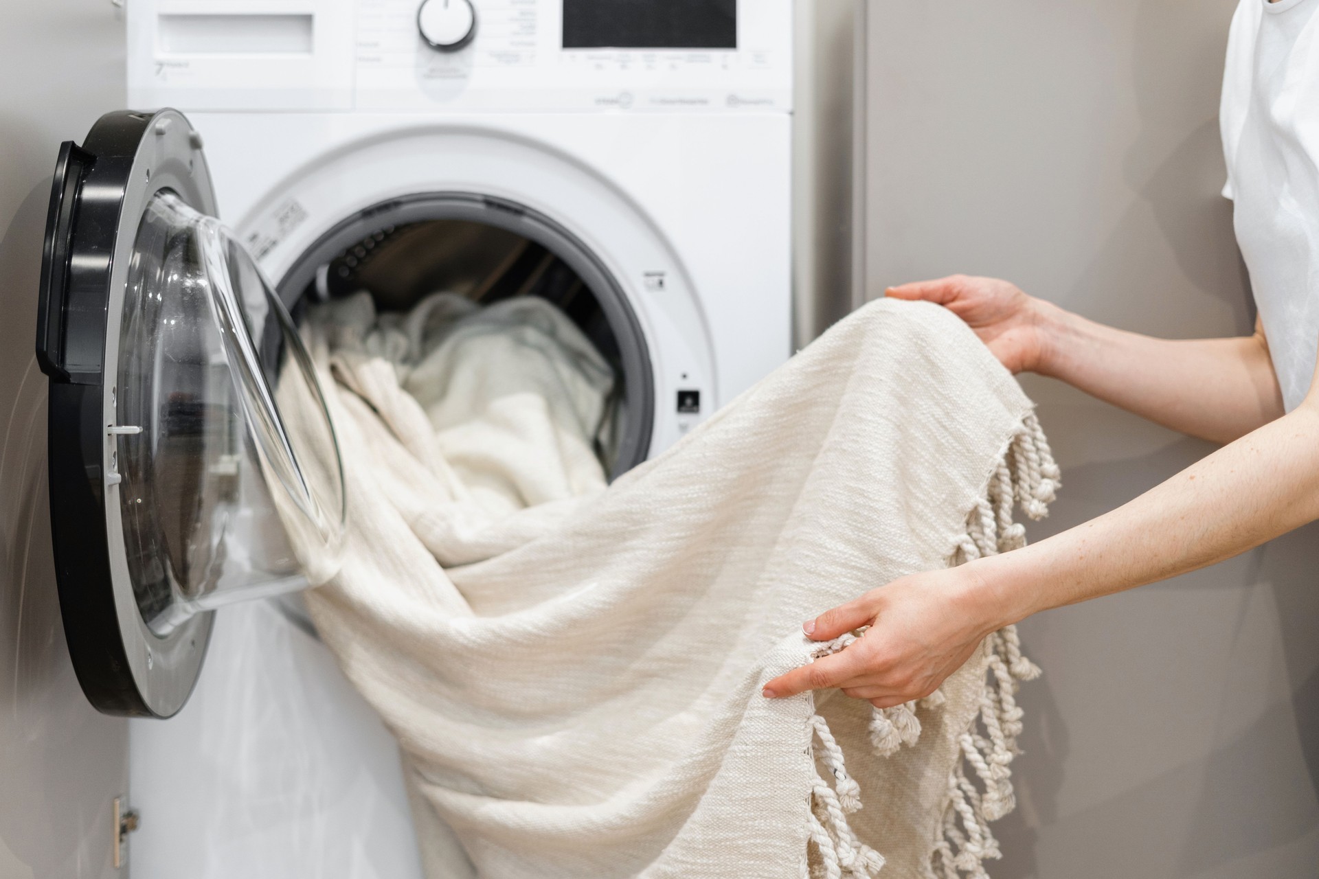 Cleaning woman unloading laundry from white washing machine