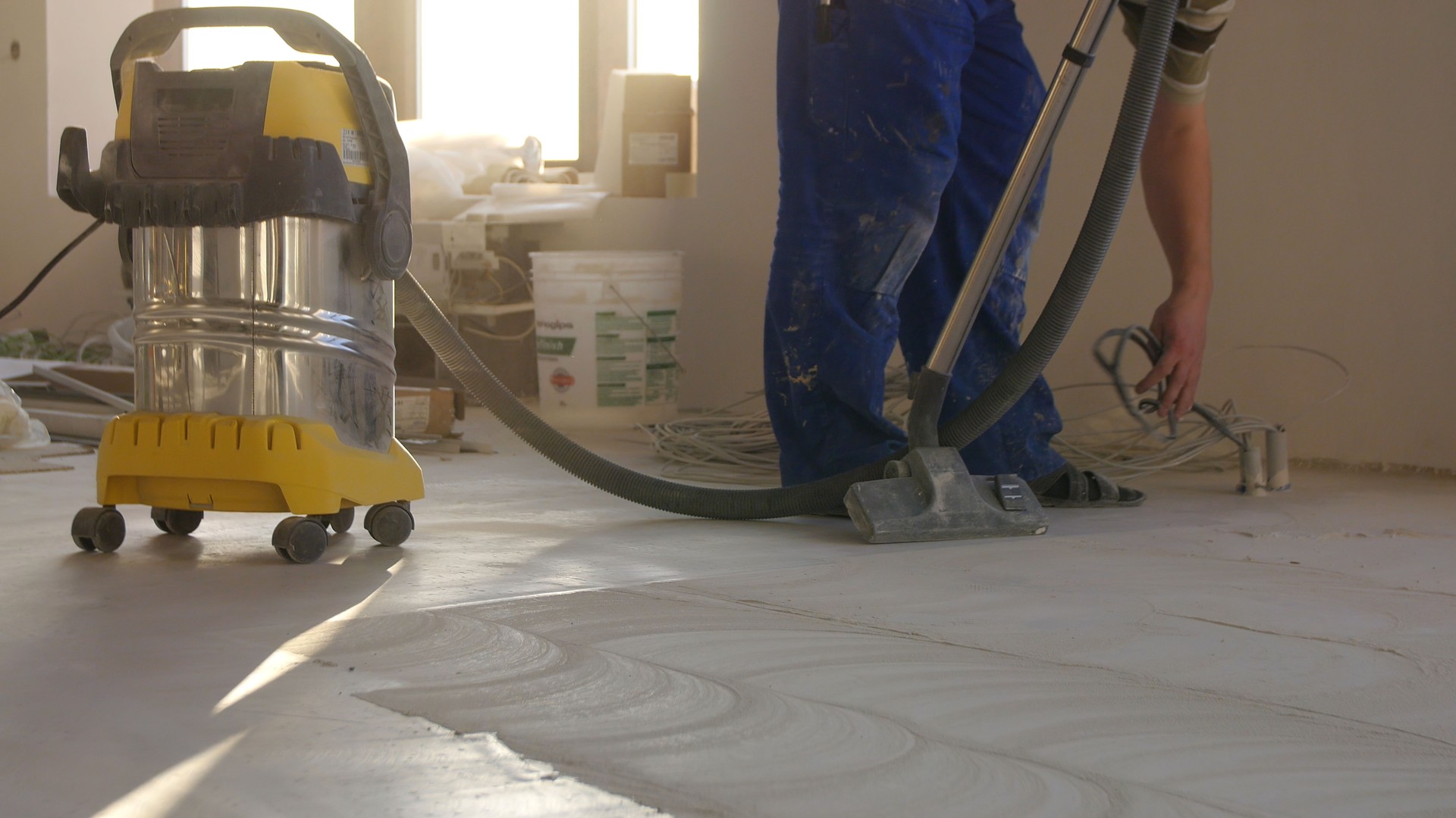 Workers in uniform cleaning room with a vacuum cleaner after installing wood parquet board during flooring work. Man vacuuming floor during repairs