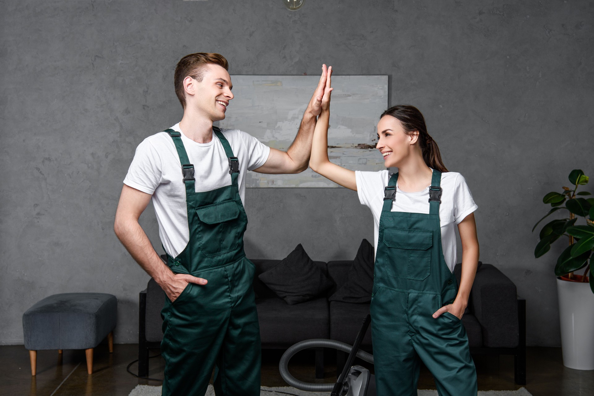 happy young professional cleaning company workers smiling each other and giving high five