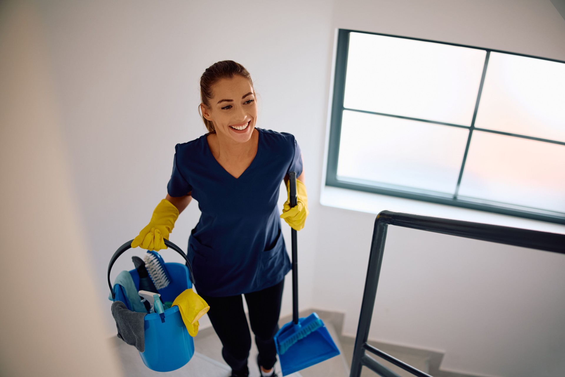 Young happy cleaning lady walking upstairs while cleaning the building.